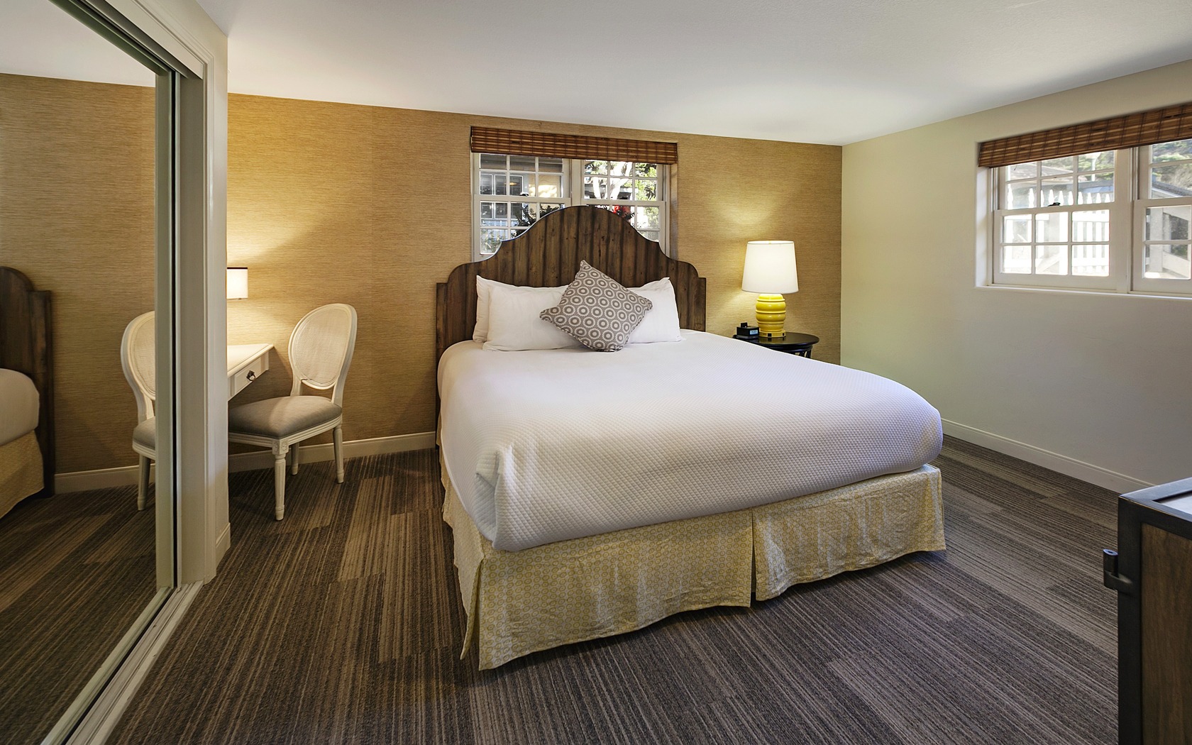 A wide-angle view of a hotel room with a large bed, chair, and mirror.