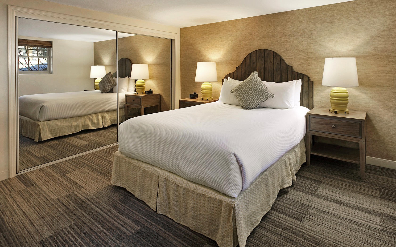 A hotel room with a bed, nightstand, and mirror