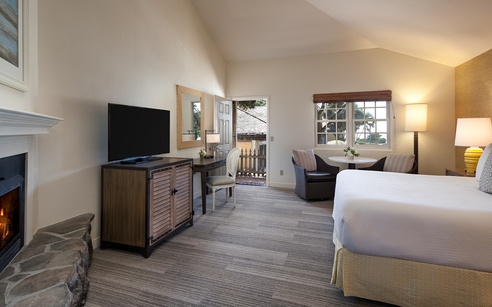 A wide view of a hotel room with a fireplace, TV, desk, seating area, and bed.
